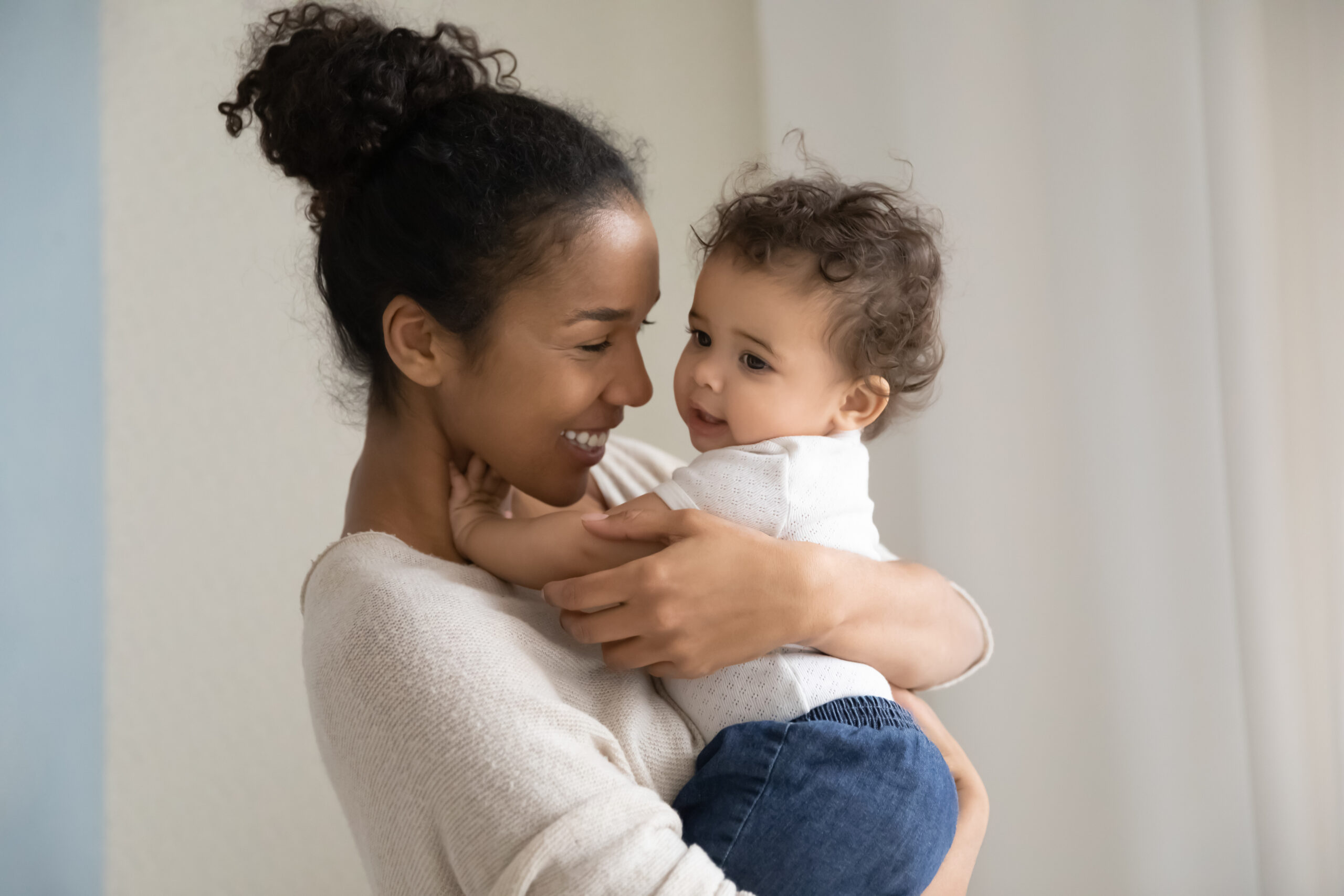 Affectionate millennial biracial mom carrying on hands funny kid.