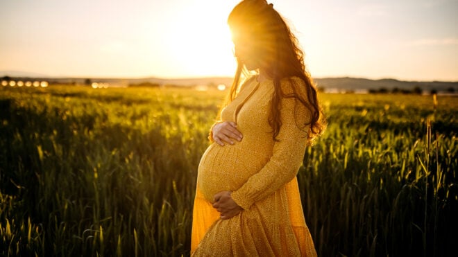 Pregnant woman holding stomach in middle of meadow