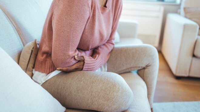 woman with arms over abdomen, postpartum pain, how long do you bleed after childbirth